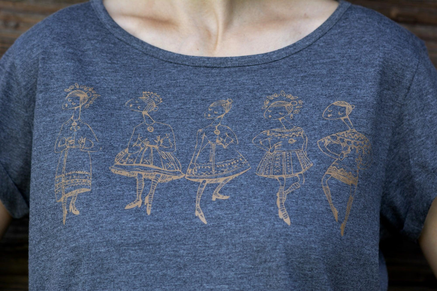 Pelēks sieviešu T-krekls tuvplānā uz kura sietspiedes tehnikā uzdrukātas piecas tautu meitenes bronzas krāsā.