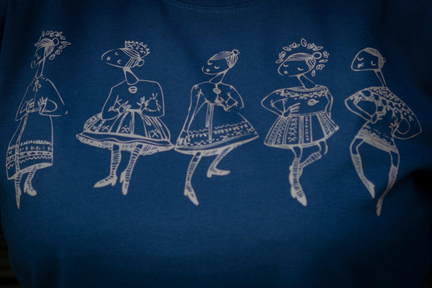 Tumši zils sieviešu T-krekls tuvplānā uz kura sietspiedes tehnikā uzdrukātas piecas tautu meitenes bronzaskrāsā.