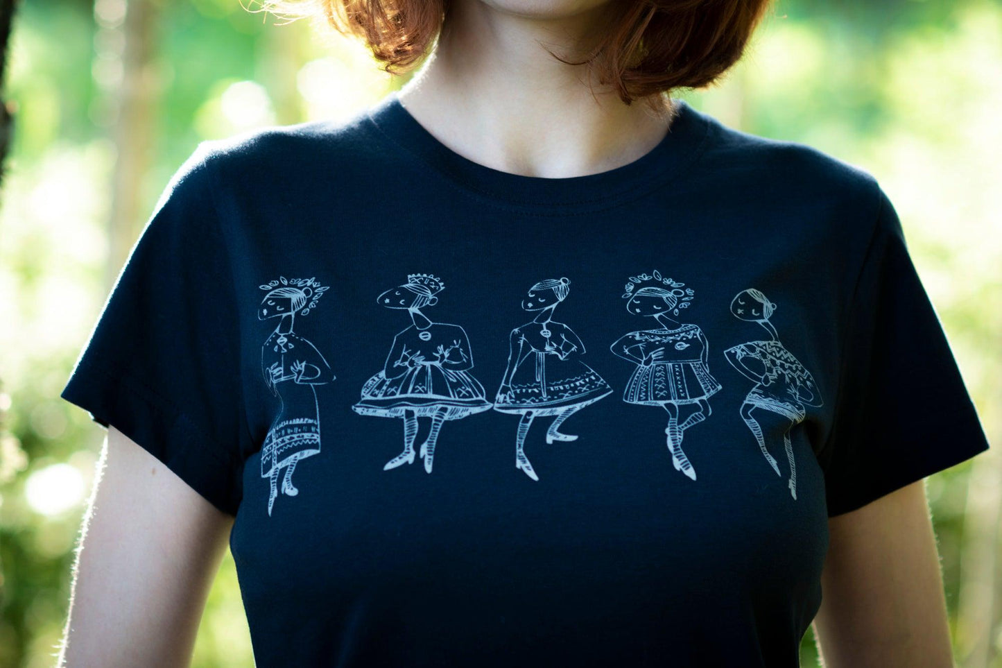 Tumši zils sieviešu T-krekls tuvplānā uz kura sietspiedes tehnikā uzdrukātas piecas tautu meitenes baltā krāsā.